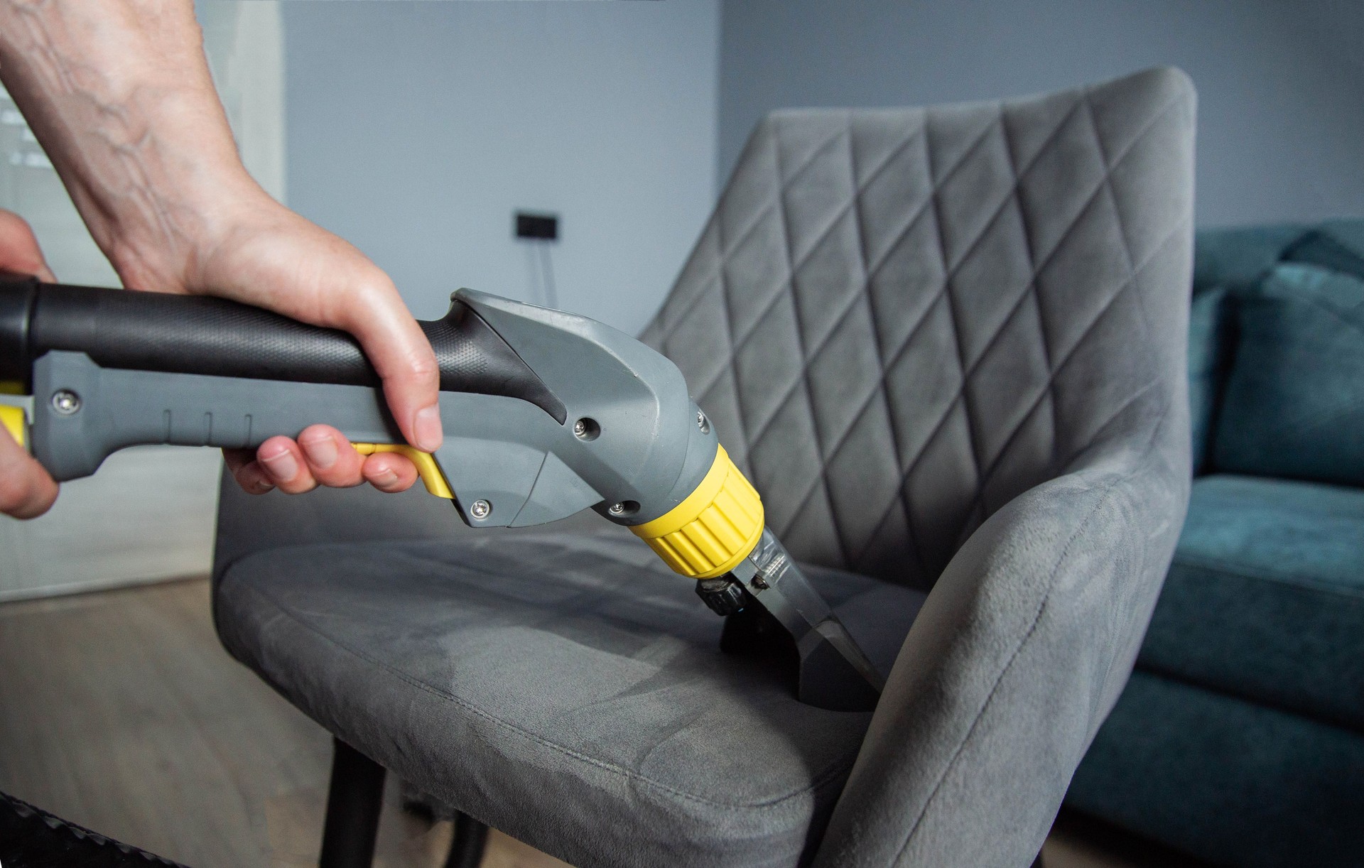 The hands of a girl with a washing vacuum cleaner clean and wash the gray upholstery of a soft chair from dirt. Cleaning services, business, close-up. Copy space for text